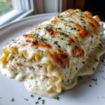 A close-up of a rich chicken alfredo lasagna roll-up covered in melted, browned cheese and parsley.