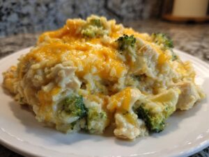 A close-up serving of creamy chicken broccoli rice casserole topped with melted cheddar cheese on a white plate.