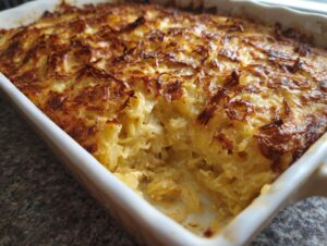 Close-up of a creamy chicken noodle casserole with a deeply browned, crispy top layer in a white baking dish.