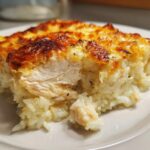 Close-up of a slice of creamy chicken and rice casserole with a golden, bubbly cheese topping.