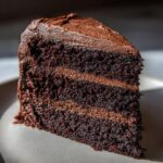 Close-up of a moist, three-layer chocolate slice of capricorn cake with thick chocolate frosting.