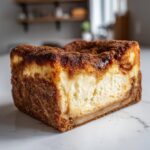 A close-up of a thick slice of churro cheesecake showing the creamy filling and heavy cinnamon sugar coating.