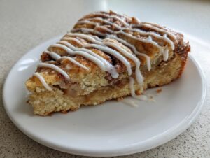 A delicious slice of cinnamon roll apple pie topped with sweet white icing drizzle, served on a white plate.