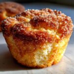 A close-up, macro shot of a freshly baked cinnamon sugar french toast muffin with a glistening, crunchy topping.
