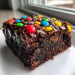A moist, fudgy square of cosmic brownies topped with melted chocolate glaze and colorful candy-coated chocolates.