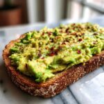 Close-up of creamy avocado toast on toasted whole-grain bread, topped generously with red chili flakes.