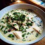 Close-up of a white bowl filled with creamy coconut soup featuring shredded chicken, mushrooms, and topped generously with fresh chopped parsley.