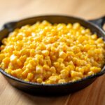 Close-up of creamy corn side dish served hot in a small black cast iron skillet.