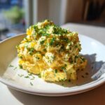 A mound of creamy, yellow egg salad recipe generously topped with freshly chopped green chives on a white plate.