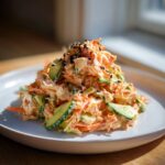 A mound of creamy kani salad mixed with shredded imitation crab, cucumber, and topped with black sesame seeds.