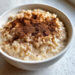 Close-up of a creamy rice pudding recipe served in a white bowl, generously dusted with ground cinnamon.