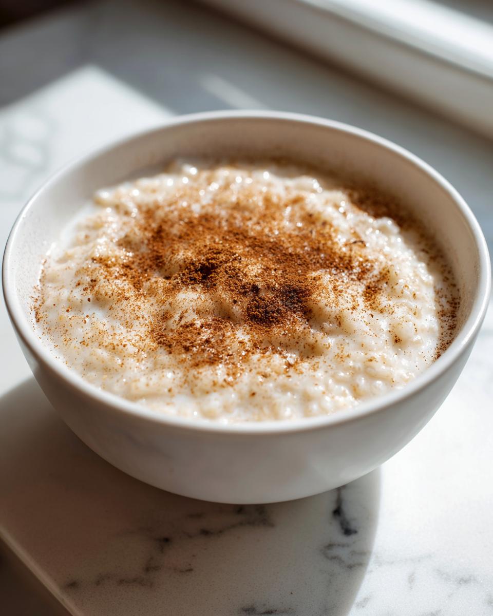 A close-up of a white bowl filled with creamy rice pudding recipe, generously dusted with cinnamon.