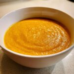 Close-up of a bowl filled with thick, vibrant orange squash soup.