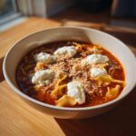 A bowl of rich, red crockpot lasagna soup topped with dollops of ricotta cheese and grated parmesan.