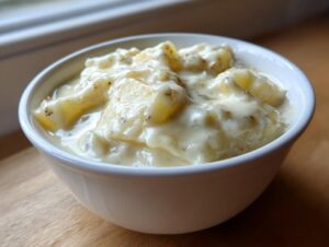 Close-up of thick, creamy easy crockpot potato soup chunks in a white bowl on a wooden surface.