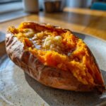 Close-up of a fluffy baked sweet potatoes split open, topped with melting butter and pepper.