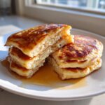 Close-up of a stack of fluffy banana pancakes cut open, drizzled with golden syrup.