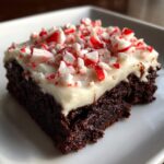 A single, fudgy square of peppermint brownies topped with thick white frosting and crushed candy canes.