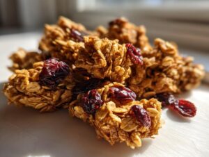 Close-up of crunchy clusters of homemade gingerbread granola mixed with dried cranberries, highlighted by sunlight.