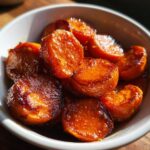 Close-up of glossy, caramelized candied sweet potatoes slices served in a small white bowl.
