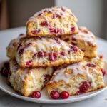 A stack of freshly baked cranberry scones topped with white glaze, garnished with whole cranberries.