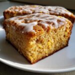 A close-up, appetizing shot of a square slice of moist lemon brownies topped with a bright white glaze.