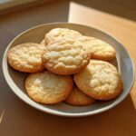 A stack of freshly baked, slightly crinkled sugar cookies piled high on a light gray plate.