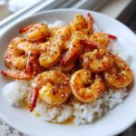 Close-up of juicy Hawaiian garlic shrimp coated in a savory glaze and served over white rice in a bowl.