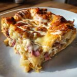 Close-up of a golden brown slice of homemade Reuben bake with melted cheese and dressing drizzle.