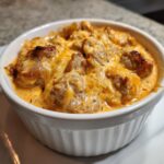 Close-up of a bubbling, hot sausage cheese dip topped with melted cheddar cheese in a white ramekin.