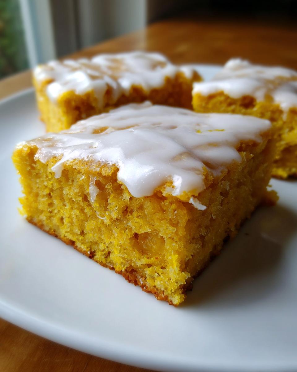 A close-up of a bright yellow, moist square of lemon brownies topped with thick white glaze.
