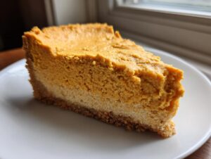 A thick, creamy slice of keto pumpkin cheesecake with a visible crust, served on a white plate.