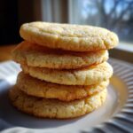A tempting stack of four golden brown sugar cookie rounds coated in sparkling sugar, resting on a white plate.