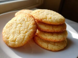 A stack of five golden brown sugar cookie rounds coated in sparkling granulated sugar, resting on a white plate.
