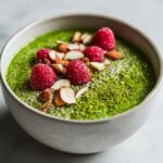 Close-up of bright green matcha chia pudding topped with fresh raspberries, sliced almonds, and matcha powder.