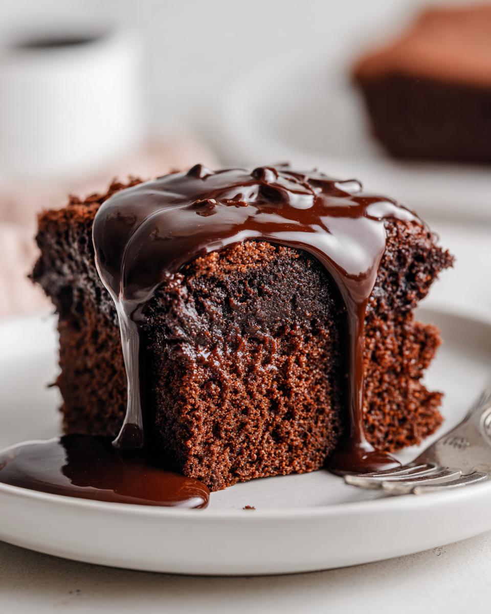 Close-up of a rich, moist slice of chocolate pudding cake being generously covered in glossy, dark chocolate fudge sauce.