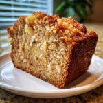 Close-up of a moist slice of hawaiian banana bread showing chunks of pineapple and nuts on a white plate.