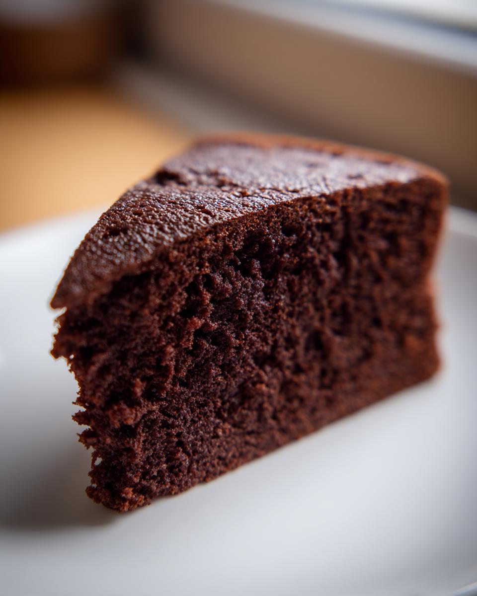 Close-up of a rich, dark slice of moist chocolate cake recipe served on a white plate.
