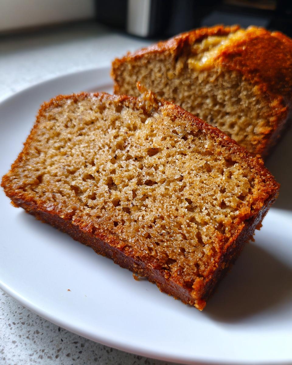 Close-up of a moist slice of sugar free banana bread showing its rich brown crumb texture on a white plate.