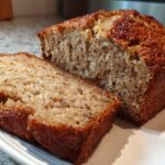 Close-up of a moist loaf of sugar free banana bread, with one thick slice cut and resting beside the main loaf.