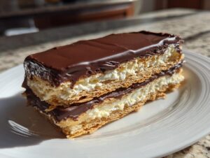 A layered slice of no-bake eclair cake featuring graham crackers, creamy filling, and chocolate frosting, served on a white plate.