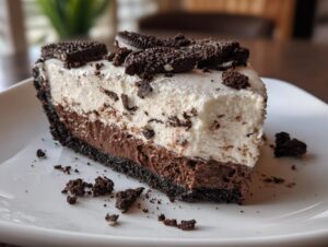 A thick slice of no bake Oreo pie showing a dark crust, chocolate layer, and white cream topping, garnished with cookie pieces.