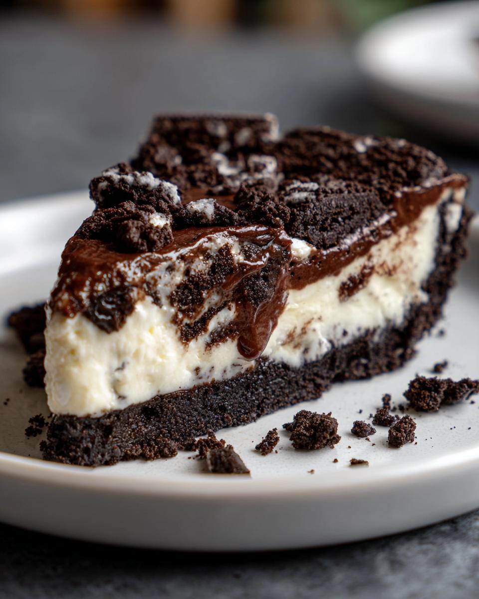 Close-up of a rich slice of no bake Oreo pie featuring a dark crust, creamy white filling, and chocolate topping.
