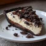 A thick slice of no bake Oreo pie showing a dark crust, chocolate layer, creamy white filling, and crushed cookie topping.