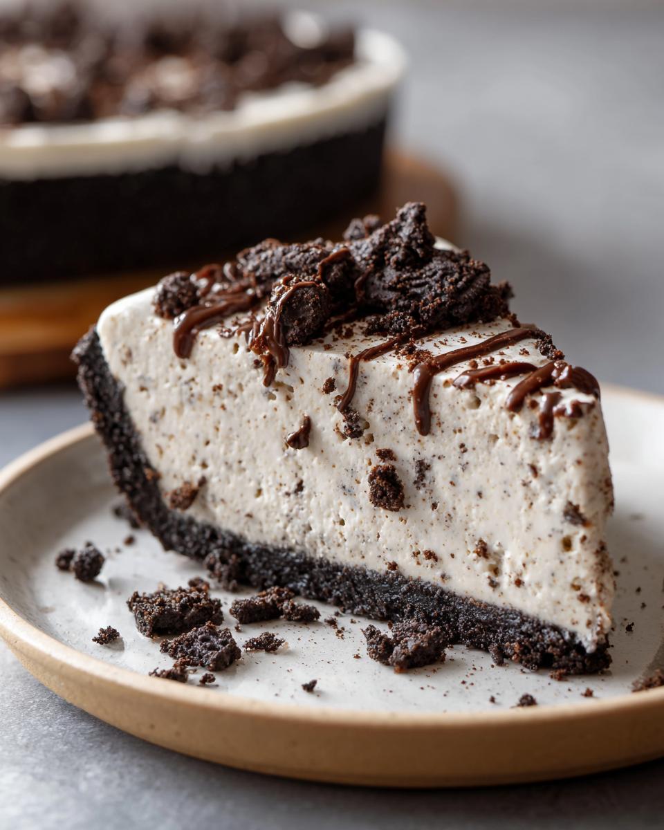 A decadent slice of no bake Oreo pie with a thick cookie crust, creamy filling, and topped with crushed cookies and chocolate syrup.