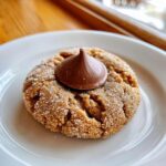 Close-up of a freshly baked peanut butter blossom cookie rolled in sugar with a chocolate kiss pressed on top.