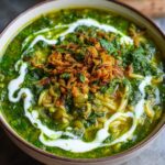 Close-up of a rich, green persian noodle soup topped with fried onions and a swirl of yogurt.