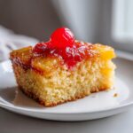 A moist slice of pineapple upside down cake topped with caramelized pineapple and a bright red maraschino cherry.