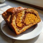 Two thick slices of vibrant orange pumpkin sourdough bread with a cinnamon swirl, resting on a white plate.