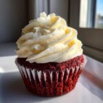 A single, vibrant red velvet cupcake topped with a swirl of thick cream cheese frosting.